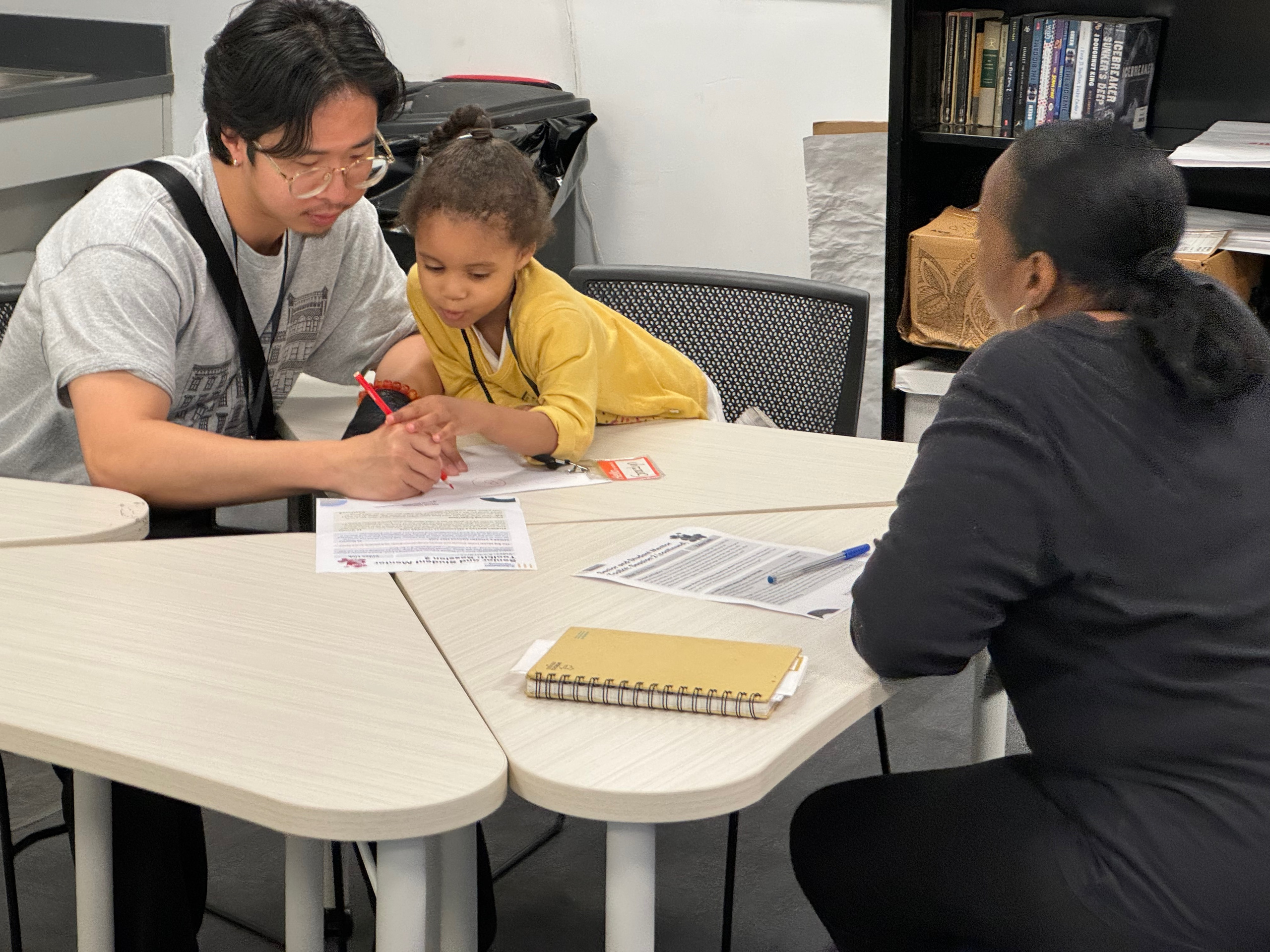 Mentor and child drawing together while an older adult looks on