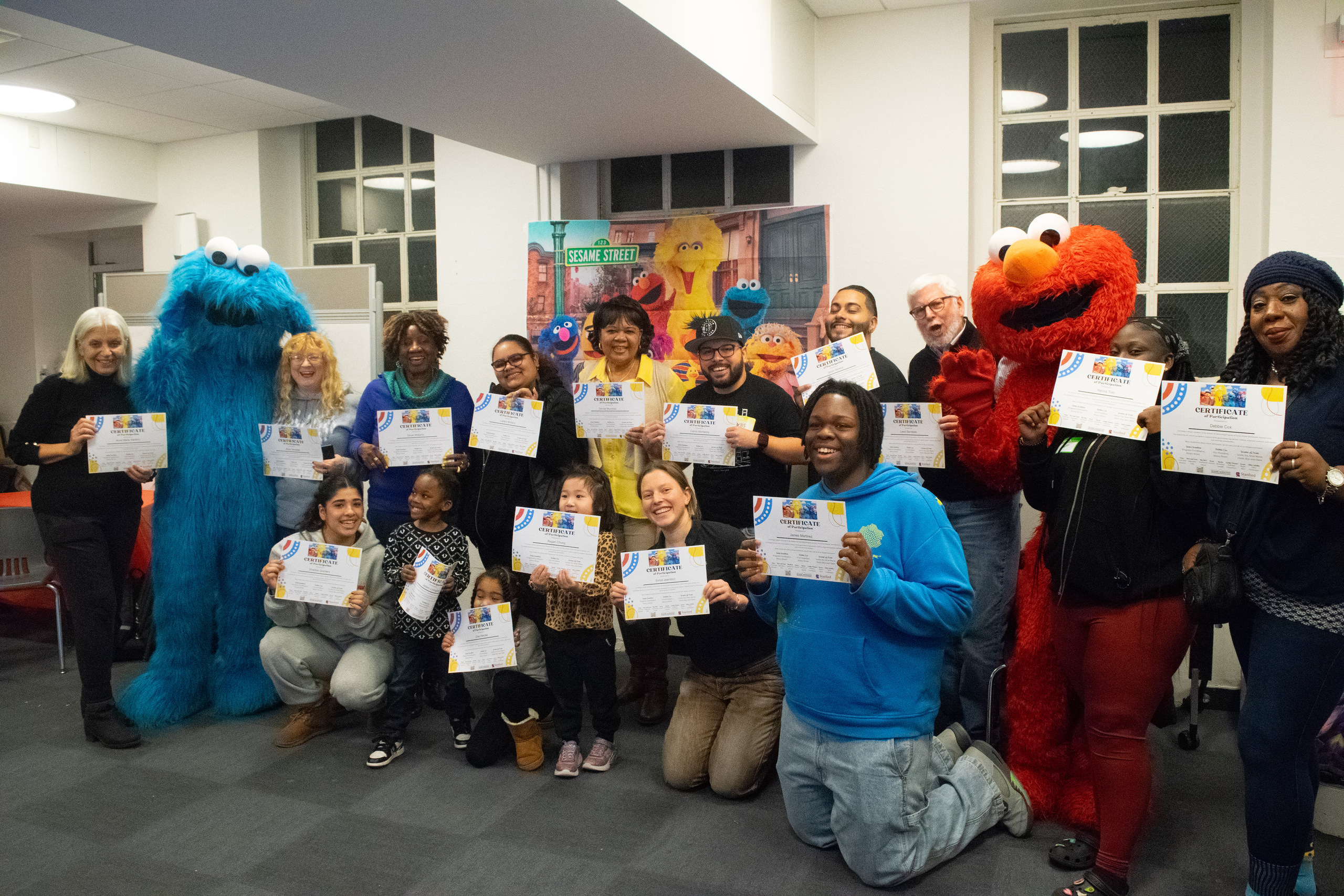 Participants of all ages holding certificates with Cookie Monster and Elmo